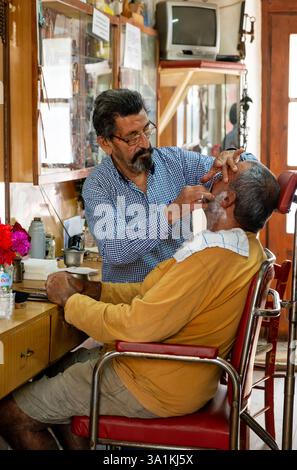 Un homme de barbier âgé rase un homme barbu dans un barbier vintage sur l'île grecque de Crète Banque D'Images