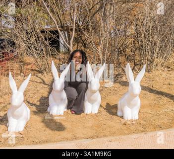 Jeune femme noire assise à côté de grandes statues de lapin blanc dans un parc. Prise à Daejeon, Corée du Sud, Asie Banque D'Images