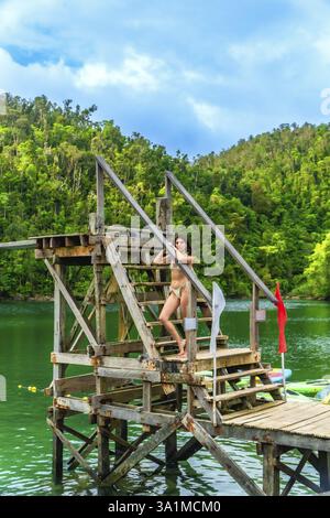 Jeune femme debout sur une plate-forme de plongée en bois à la lagune de sugba dans l'île de Siargao, philippines, profitant de l'eau turquoise et de la végétation luxuriante Banque D'Images