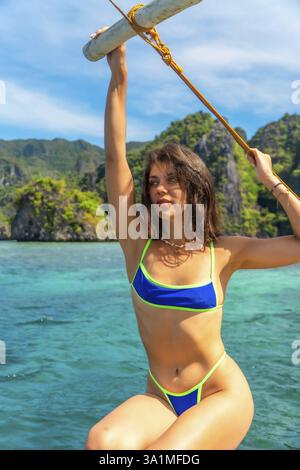 Jeune femme tenant un poteau en bois sur un bateau banca, naviguant à travers les eaux turquoises de l'île de coron, philippines, par une journée ensoleillée Banque D'Images