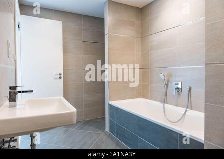 Intérieur minimaliste de la salle de bains avec baignoire blanche, lavabo mural et robinet chromé. Banque D'Images