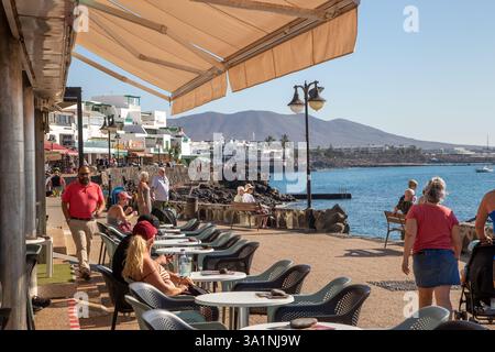 Les gens apprécient le soleil d'hiver de février dans les bars et cafés le long du port de la station balnéaire des Canaries de Playa Blanca Lanzarote Espagne Banque D'Images