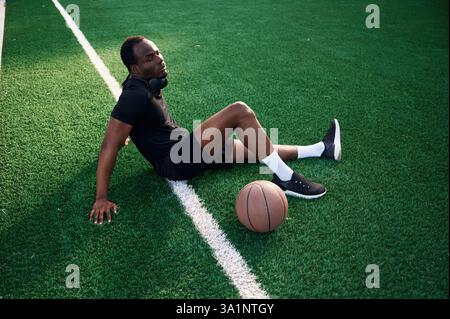 Assis et relaxant. Le jeune homme noir est avec un ballon de basket-ball à l'extérieur. Banque D'Images