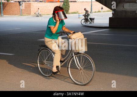 Femme portant une visière à vélo tout en parlant sur un téléphone portable à Tianjin, Chine. Banque D'Images