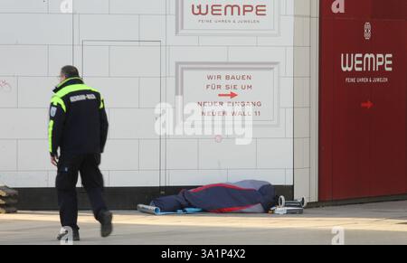 Ein Obdachloser liegt in seinem Schlafsack vor dem Juwelier Wempe am Jungfernstieg, der gerade umgebaut wird. Ein Mitarbeiter der Hochbahn-Wache geht an dem schlafenden Mann vorbei. Altstadt Hamburg *** Un sans-abri est allongé dans son sac de couchage devant la bijouterie Wempe sur Jungfernstieg, qui est en cours de rénovation. Un membre de la garde Hochbahn passe devant l'homme endormi Altstadt Hamburg Banque D'Images