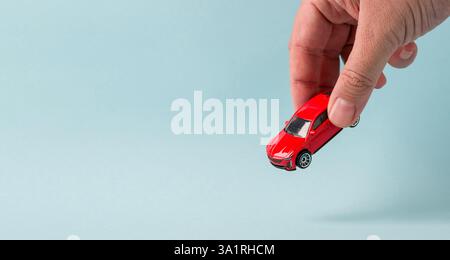 Main tenant une voiture jouet rouge sur un fond bleu clair Banque D'Images