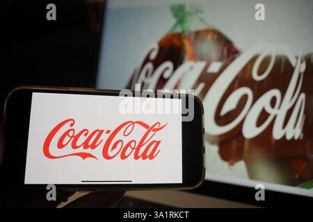 Roosendaal, pays-Bas - 10 mars 2025 : un téléphone portable affichant le logo de Coca-Cola, avec le site Web de l'entreprise et le produit en arrière-plan. Banque D'Images