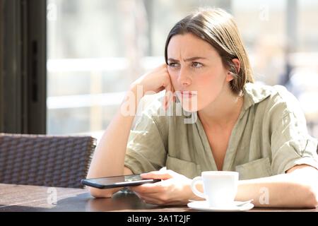 Femme en colère se plaignant dans un bar tenant le téléphone et pensant détourner le regard Banque D'Images