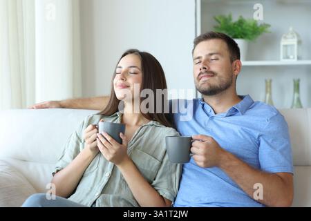 Couple heureux boire et respirer relaxant assis dans un canapé à la maison Banque D'Images