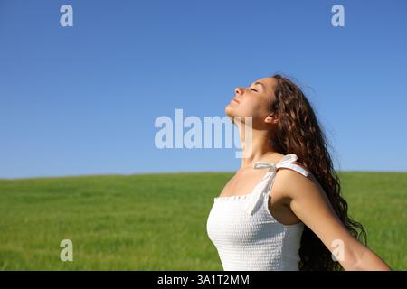 Femme en robe blanche respirant l'air frais dans le champ vert une journée ensoleillée dans la nature Banque D'Images