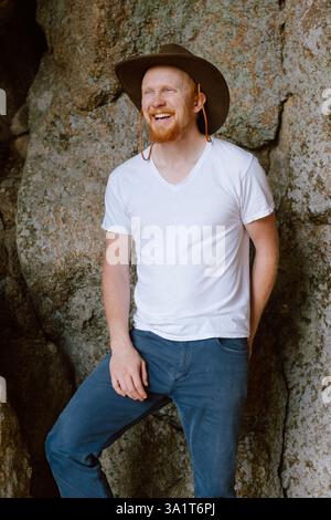 Homme souriant en chapeau de cow-boy et chemise blanche appuyé contre les rochers Banque D'Images