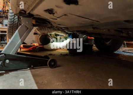 Mécanicien professionnel fixant les problèmes de voiture sous le véhicule à l'aide du cric hydraulique dans l'atelier automobile. Banque D'Images