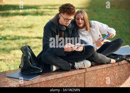Jouer à des jeux à l'aide de smartphones. Deux jeunes étudiants sont ensemble à l'extérieur. Banque D'Images