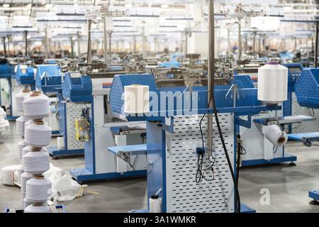 Vue de machines automatisées de fabrication de textiles dans une usine, avec des bobines de fil blanc prêtes pour le traitement. Banque D'Images