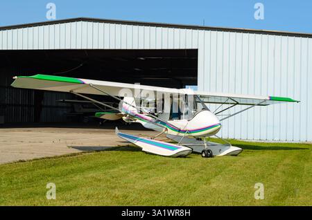 Avion à flotteur monomoteur stationné sur l'herbe devant un hangar avec un ciel bleu clair. Banque D'Images