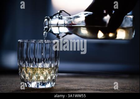 Verser une boisson à partir d'une bouteille transparente swing-top dans un verre dans une pièce sombre Banque D'Images