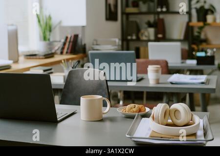 Plan moyen du lieu de travail vide du programmeur avec ordinateur portable noir, écouteurs et déjeuner sur le bureau Banque D'Images