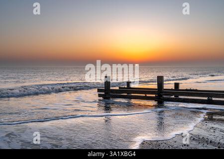Lever de soleil sur la plage à Mundesley, Norfolk, Royaume-Uni avec un groyne en bois que la marée recule Banque D'Images