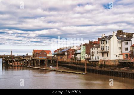 Vue sur le paysage urbain de Whitby avec des bâtiments, une jetée et de l'eau sous un ciel nuageux. Banque D'Images