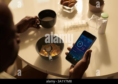 Angle élevé de l'homme mûr assis à table tout en mangeant du muesli avec du lait et en regardant à travers l'indice de qualité du sommeil sur l'écran du smartphone Banque D'Images