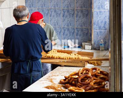 Deux personnes travaillant dans une cuisine de boulangerie, façonnant des bretzels sur une table en bois avec des bretzels finis à proximité Banque D'Images