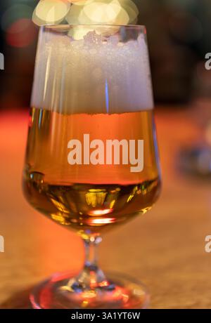 Une photographie rapprochée d'un verre rempli de bière ambre, mettant en évidence sa riche couleur et sa tête mousseuse sur un fond légèrement flou Banque D'Images