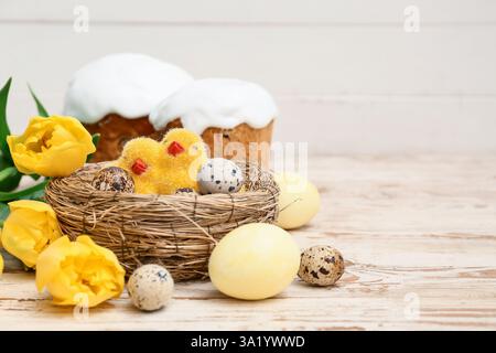 Gâteaux de Pâques sucrés avec des œufs, des poussins et de belles fleurs de tulipe sur fond de bois blanc Banque D'Images