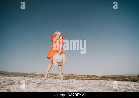 Femme dans une robe rouge debout sur un rocher avec ciel bleu Banque D'Images