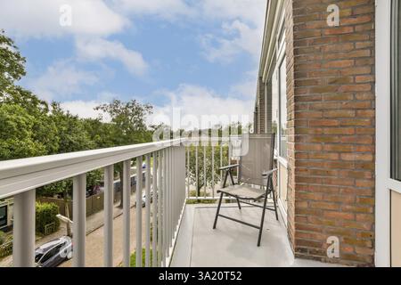 Une scène de balcon charmant avec une chaise confortable, donnant sur une végétation luxuriante et un ciel bleu clair, parfait pour se détendre et profiter de la nature. Banque D'Images