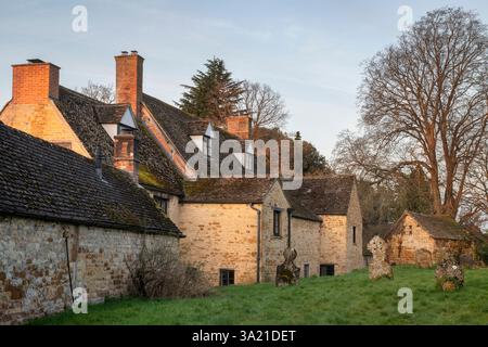 Maisons faisant marche arrière sur le cimetière dans la lumière tôt le matin..Barton on the Heath. Warwickshire. Angleterre. Banque D'Images