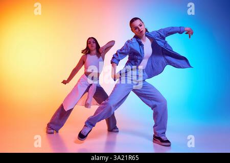 Danseurs de hip hop passionnés exécutant des mouvements synchronisés dans des tenues urbaines décontractées sous un gradient de lumière néon. Banque D'Images