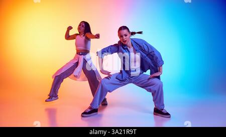 Dansez dans la rue avec de jeunes femmes confiantes en mouvement, réalisant des mouvements hip hop sous des néons. Banque D'Images