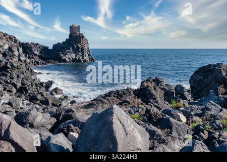 Ancienne tour côtière de Catane, Sicile, debout fièrement au milieu des roches volcaniques accidentées de lave et de la mer Méditerranée bleue profonde sous un SK clair et dynamique Banque D'Images