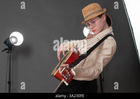 Vue latérale de belle guitariste féminine, caressant sa guitare acoustique espagnole à six cordes avec passion et regarde directement la caméra. C'est une jeune femme Banque D'Images