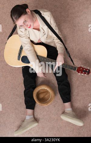 Vue en angle élevé du guitariste avec guitare, assis avec les jambes écartées et chapeau de paille devant elle, destiné à être un don pour jouer de la musique. Femme Lookin Banque D'Images