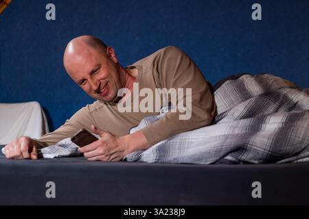 Homme au lit, regardant sur un appareil mobile. Banque D'Images