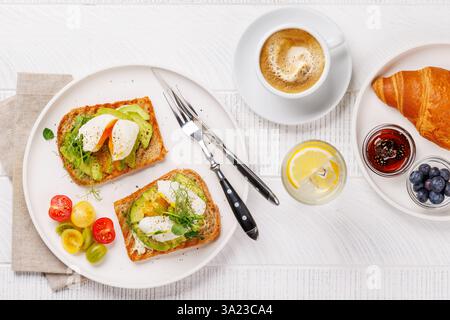 Petit déjeuner avec de délicieux toasts à l'avocat garni d'œufs pochés parfaitement cuits et croissant croustillant avec des baies et de la confiture Banque D'Images