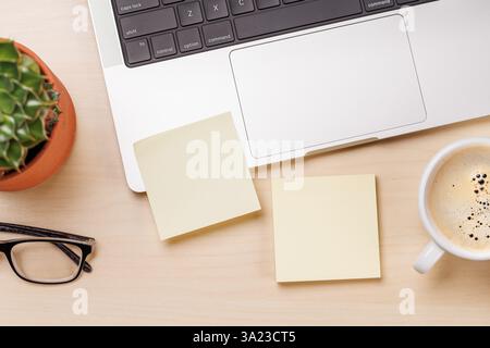 Une configuration d'espace de travail comprenant un ordinateur portable et des notes en papier autocollant vierges sur un bureau, offrant un espace de copie suffisant pour la conception ou la messagerie Banque D'Images