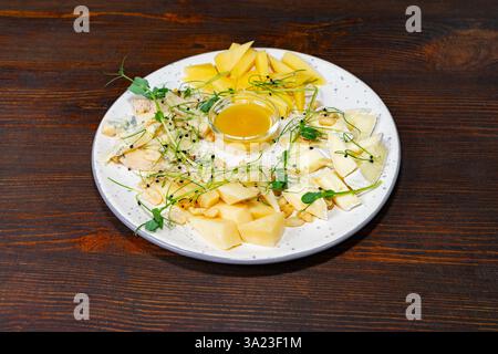 Un plateau magnifiquement arrangé avec divers fromages, des fruits frais et un petit bol de miel. Idéal pour partager lors d'un dîner cosy entre amis Banque D'Images