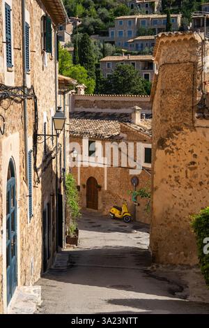 Rue étroite dans le village pittoresque Deia, Majorque, Espagne. Murs de pierre vieilles maisons, scooter jaune garé à la fin de la rue, ajoutant de la couleur. Vie urbaine, trav Banque D'Images