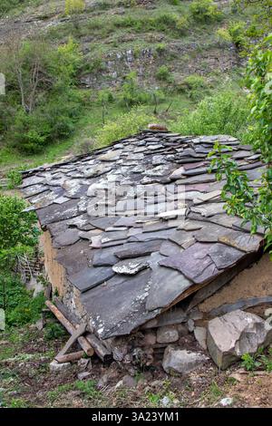L'image montre un vieux toit en pierre d'une structure rurale nichée dans une verdure luxuriante sur une colline. Le toit est fait de pierres plates et présente des signes de W. Banque D'Images