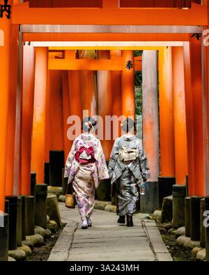 Deux femmes vêtues de vêtements japonais traditionnels en route à travers les milliers de portes torii du sanctuaire Fushimi Inari à Kyoto. Banque D'Images