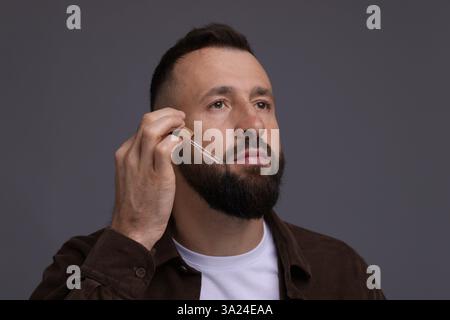 Homme appliquant du sérum sur sa barbe sur fond gris Banque D'Images