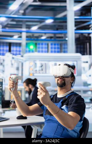 Technicien d'usine photovoltaïque utilisant le casque VR pour effectuer des essais de machines robotiques. Travailleur d'usine de panneaux solaires utilisant la réalité virtuelle pour consulter les paramètres de fabrication, faire des ajustements Banque D'Images