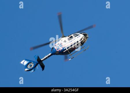 Palm Springs, Californie, États-Unis. 3 mars 2025. Cette photographie capture un hélicoptère médical Mercy Air en vol contre un ciel bleu clair. L'hélicoptère, un bimoteur Eurocopter EC135, est peint en blanc avec des accents bleus et rouges, avec le symbole reconnaissable Star of Life sur son fuselage. Le numéro d'enregistrement N58BAM est visible le long de la flèche de queue, qui porte également un autocollant de drapeau américain. L'avion est équipé d'un train d'atterrissage à patins et d'un rotor de queue fermé fenestron, une caractéristique de conception caractéristique de l'EC135. Le flou de mouvement des pales du rotor principal véhicule le R de l'hélicoptère Banque D'Images