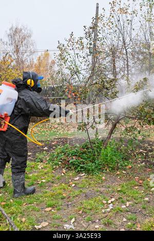 l'homme en masque et en salopette pulvérise le jardin avec des pesticides et des insecticides contre les parasites en automne. Prévention des maladies dans le jardin. Traitement saisonnier Banque D'Images