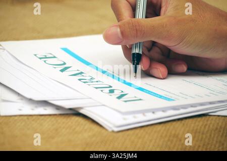 Main tenant un stylo remplissant le formulaire d'assurance sur la surface des documents. Banque D'Images