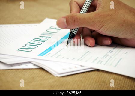 Main tenant un stylo remplissant le formulaire d'assurance sur la surface des documents. Banque D'Images