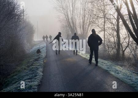 Sur le chemin de Radley Boathouse par la Tamise. Un de mes sentiers préférés, n'importe où. Il mène de mon village natal de Radley dans l'Oxfordshire, en Angleterre, à une partie pittoresque de la Tamise près de Radley Boathouse. Il parvient à paraître joli tout au long de l'année - et en particulier ici un matin d'hiver brumeux, juste après le lever du soleil. Un promeneur de chien et des joggers disparaissent dans les brumes... Banque D'Images