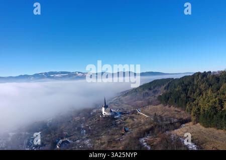 Vue aérienne du village de montagne brumeux et brumeux et tour de l'église en hiver par drone Banque D'Images